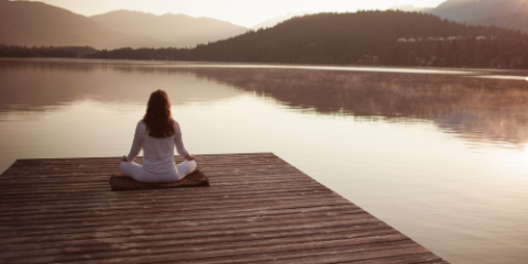 woman meditating on a dock beside a lake